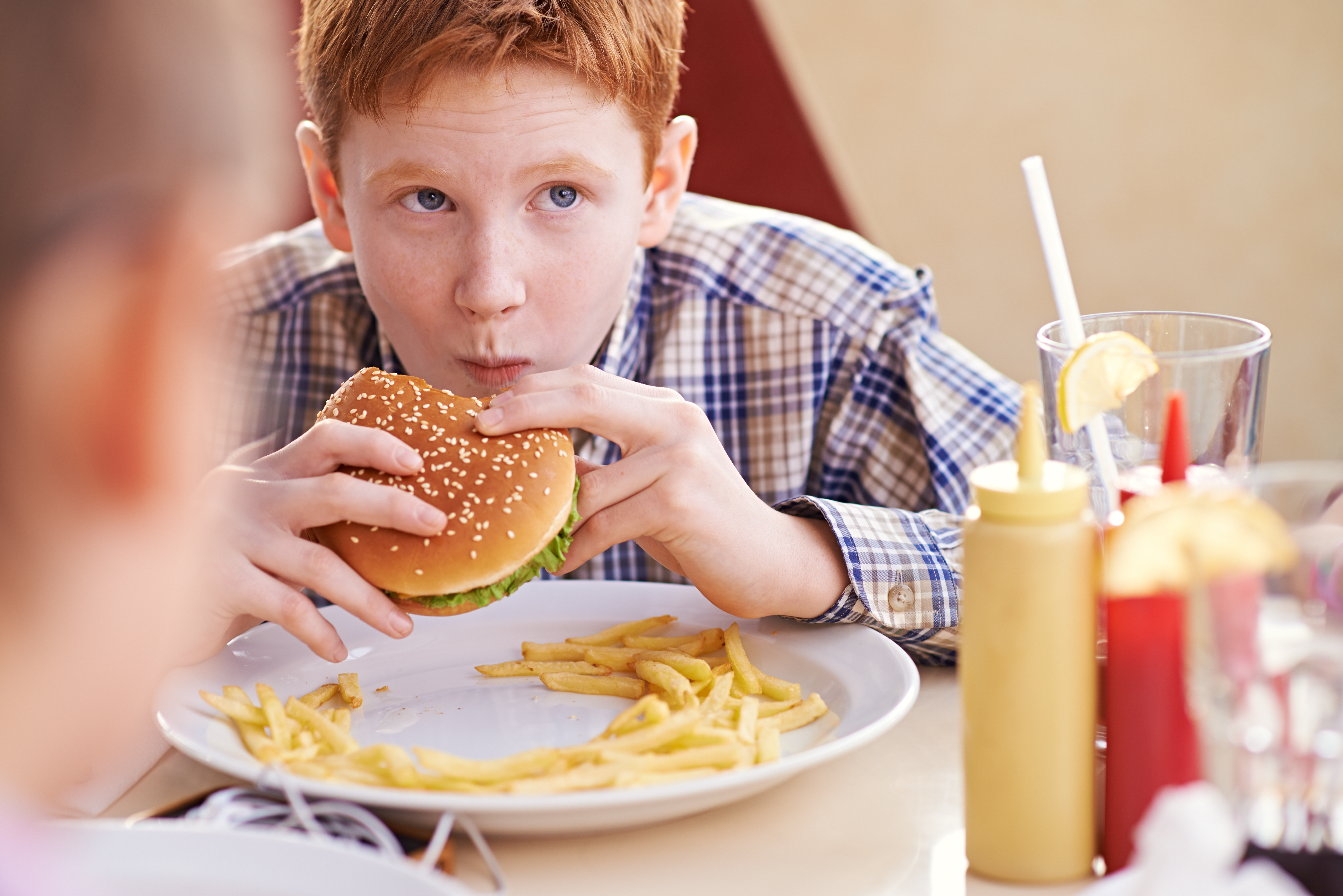 Teenage boy comfortably eating hamburger and fries Teenage boy comfortably eating hamburger and fries